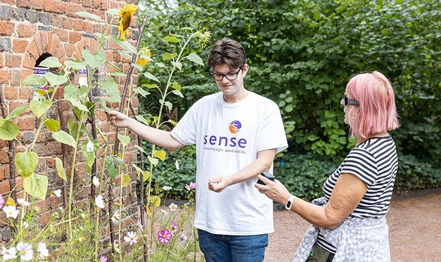 A person wearing a Sense t-shirt engages with a plant and a visitor