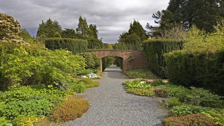 Garden with a path in the middle towards an archway in a brick wall