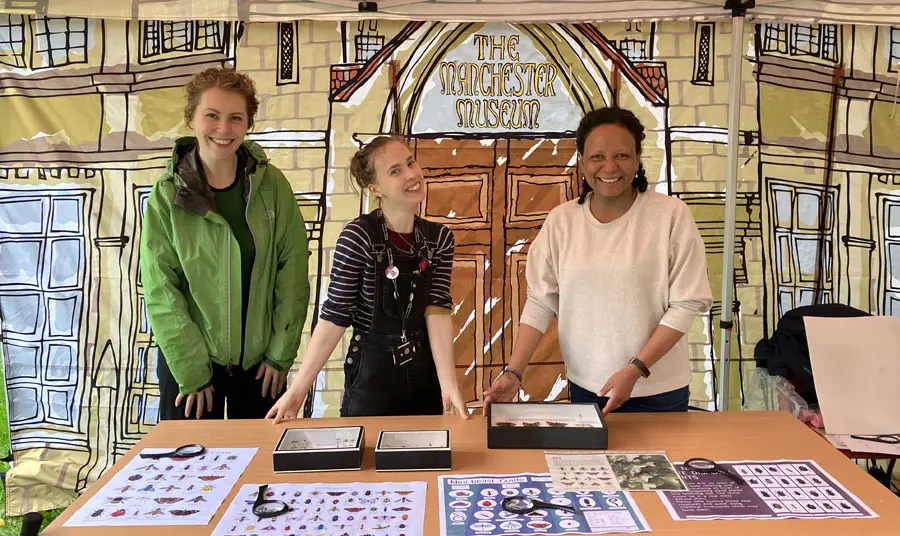 Three people at an event stand with information about insects