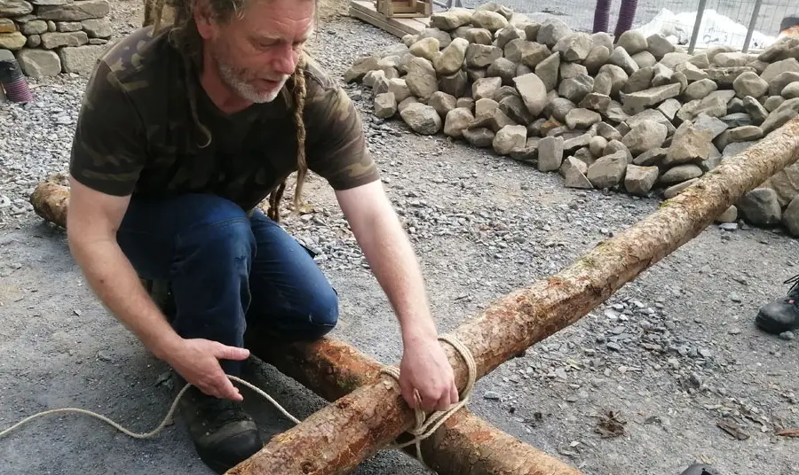 A person ties rope around logs to build the crannog