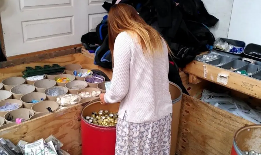 A person is standing in a scrap store looking through barrels of recycled items.