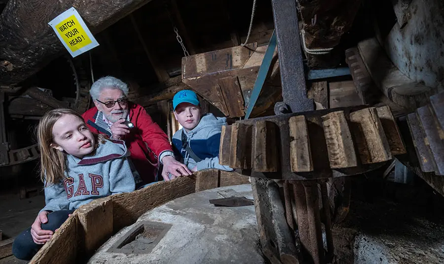 Andrew, a volunteer guide, shows young visitors the millstone inside the windmill