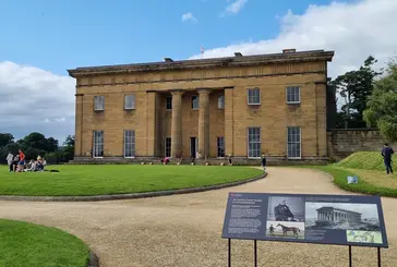 Belsay Hall with people sat on the lawn in front