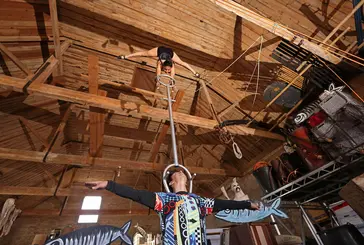 Two circus performers perform a balancing act inside a wooden barn-style building
