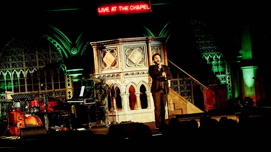 Nish Kumar performing at Union Chapel in front of pulpit and Live at the chapel LED sign