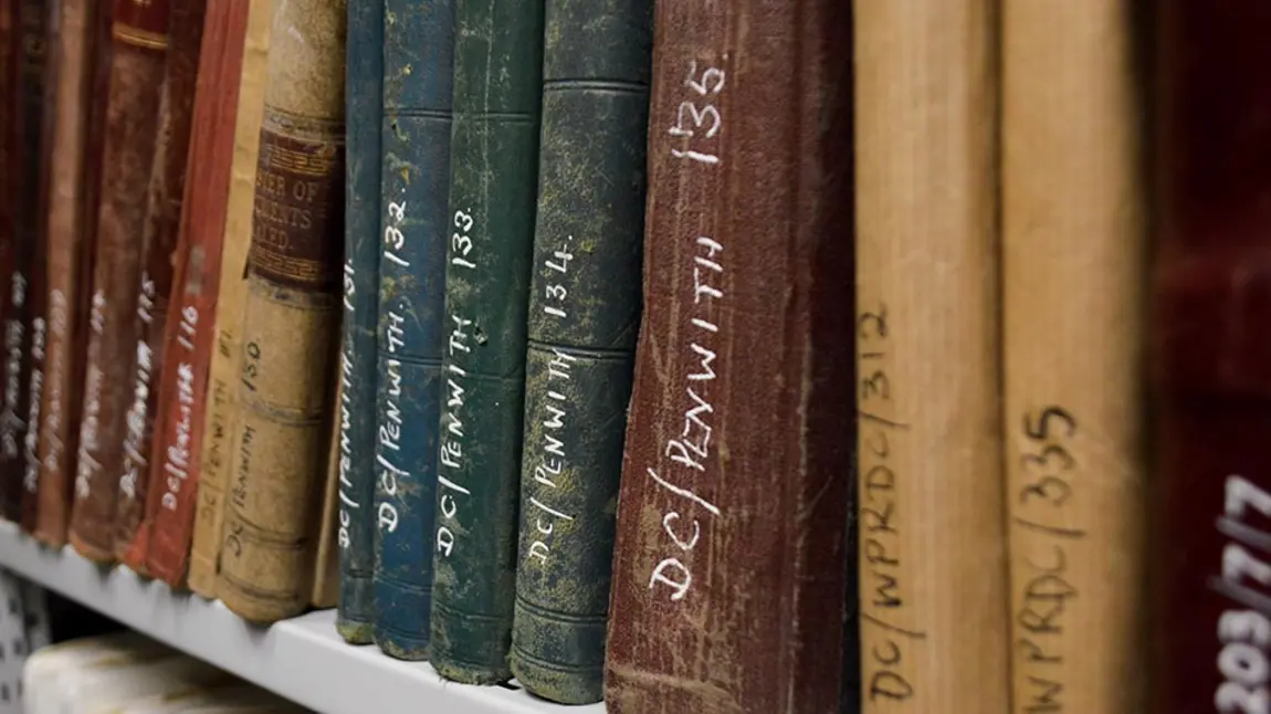 A bookshelf of old books in an archive. The books have reference numbers written on their spines.