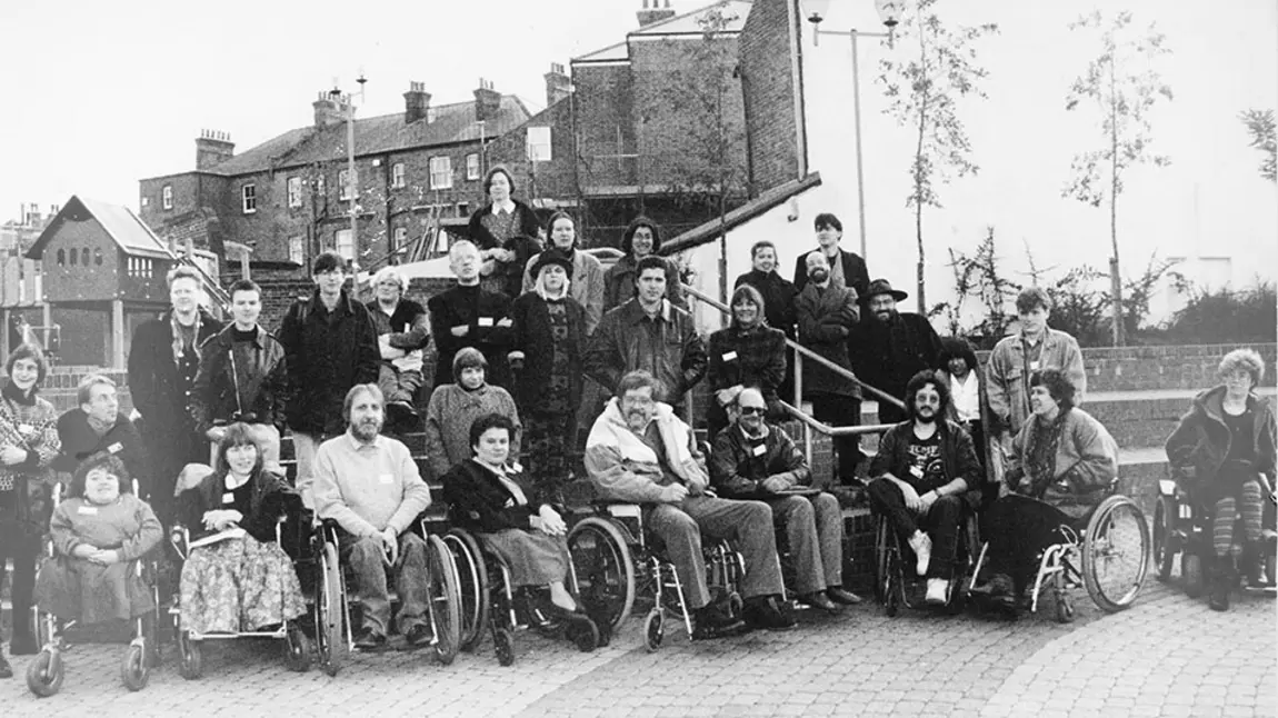 A black and white group photo of about 30 people. The front row of people are using wheelchairs, with others standing on steps behind them.