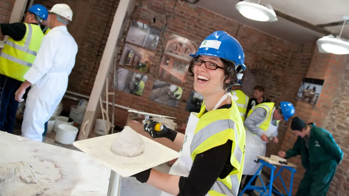 A smiling woman holding a board with plaster on it and a trowel