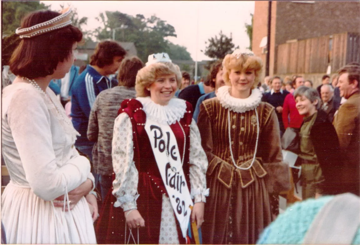 Three people at a busy fair dressed like Queen Elizabeth I, with ruffles, dresses and crowns